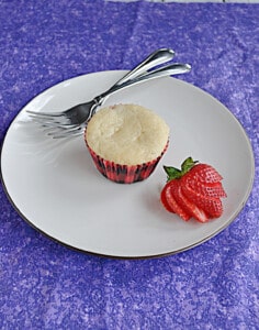 A plate with a muffin, a strawberry, and two forks on it.
