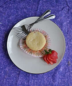 Top view of a muffin with the paper peeled off, two forks, and a sliced strawberry.