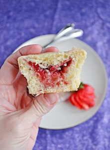 A close up of a hand holding half a muffin with strawberry jam in the middle.
