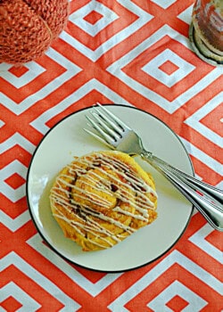 A close up of a cinnamon roll on a plate with glaze drizzled on top.