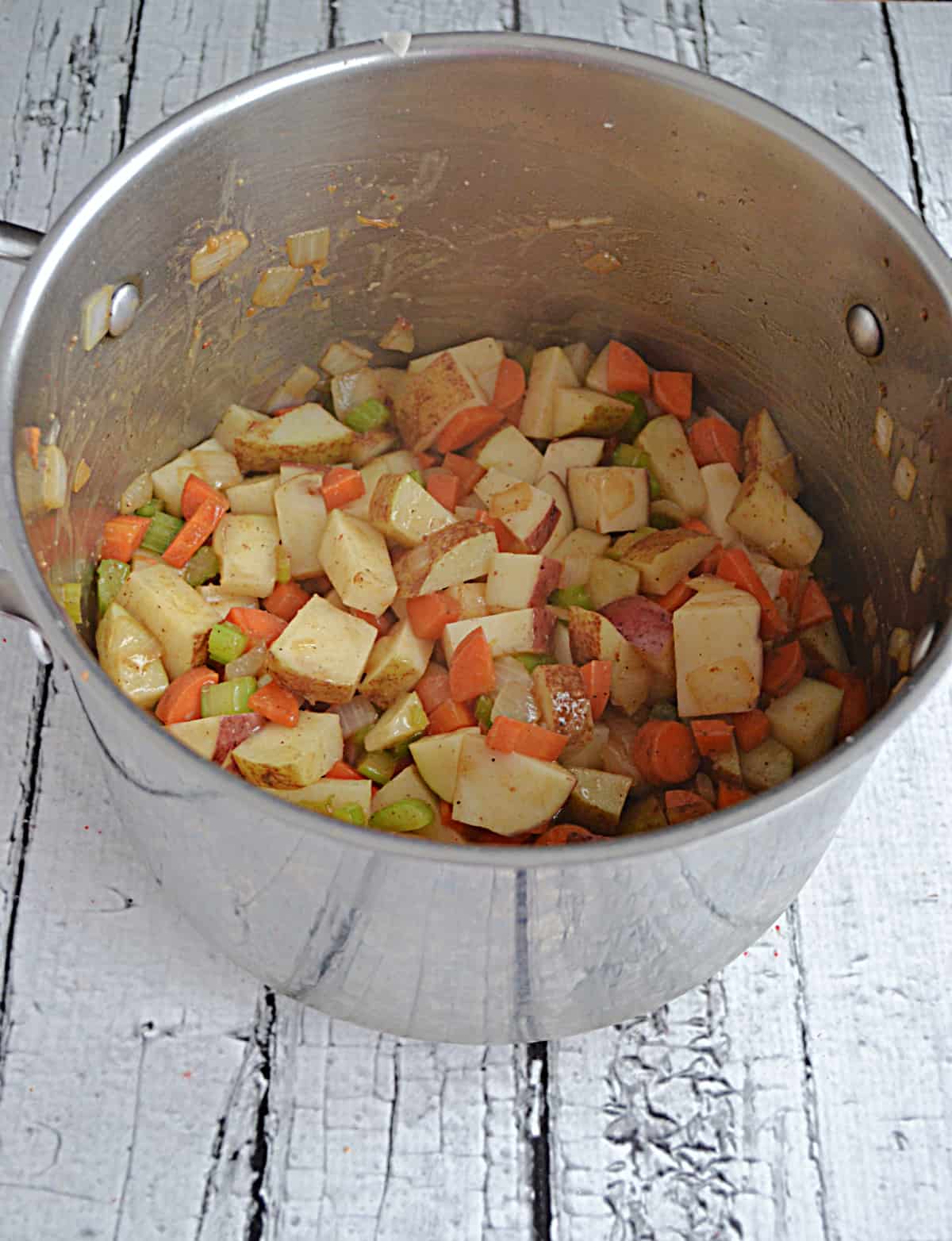 A soup pot with celery, carrots, and potatoes in it. 