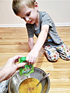 A picture of a 4 year old boy squeezing applesauce into cupcake batter.