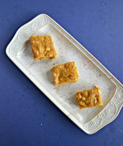 A white platter sitting diagonally with 3 blondies sitting on the platter on a blue background.