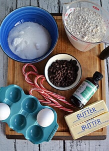 A cutting board with ingredients for making peppermint bark cookies.