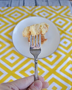 A fork with a bite of baked pineapple on it and a plate in the background.