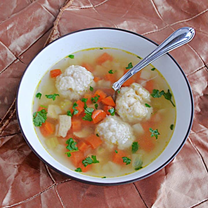 A bowl of Chicken Dumpling Soup with three large dumplings in it as well as a spoon.