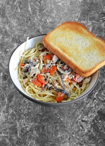 A bowl of Linguini and Clams with a slice of garlic bread in the bowl.