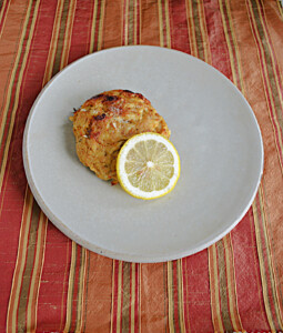 A plate with a golden brown crab cake with a lemon wedge.