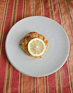 A plate with a crab cake and a lemon slice on top.