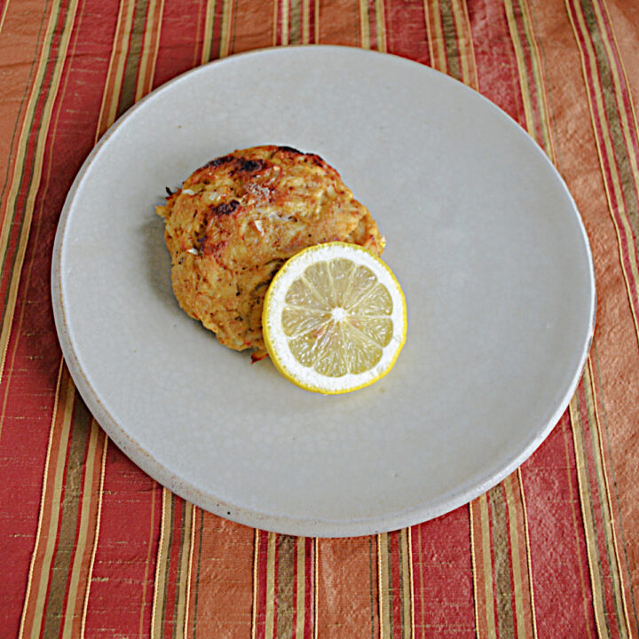 A plate with a golden brown crab cake with a lemon wedge.