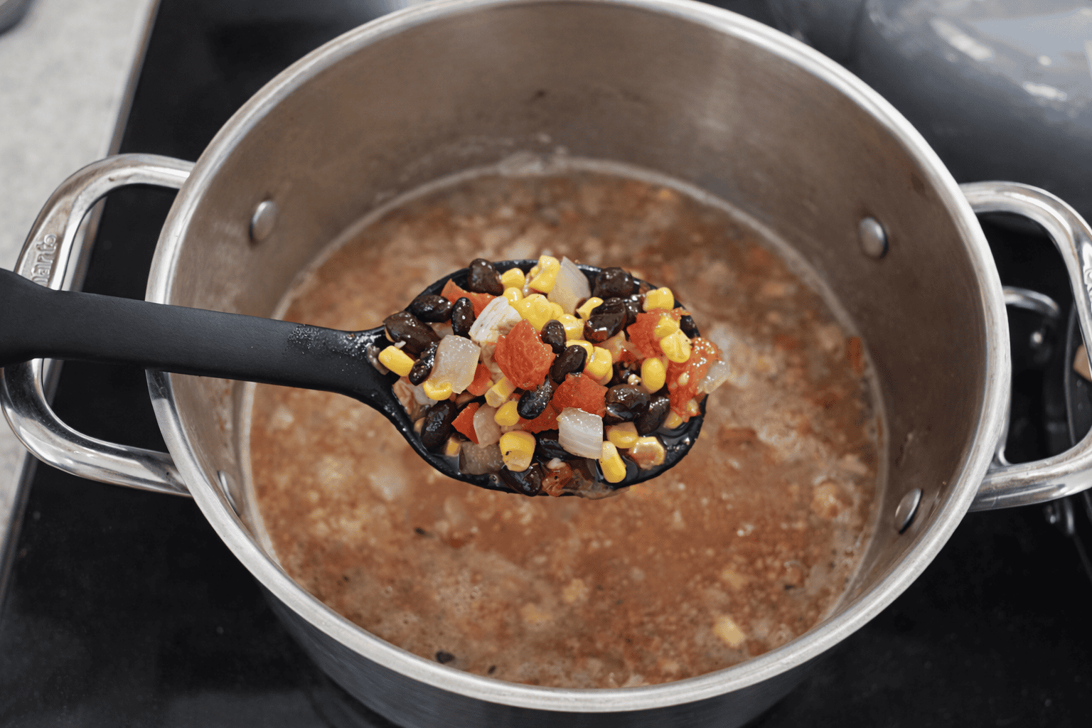 A soup pot with a spoon holding a large scoop of soup on it.
