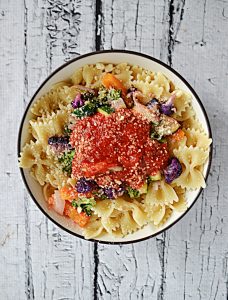 A bowl of bow tie pasta covered in sauteed vegetables and topped with a scoop of marinara sauce.