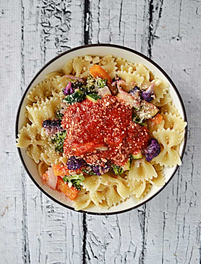 A bowl of bow tie pasta covered in sauteed vegetables and topped with a scoop of marinara sauce.