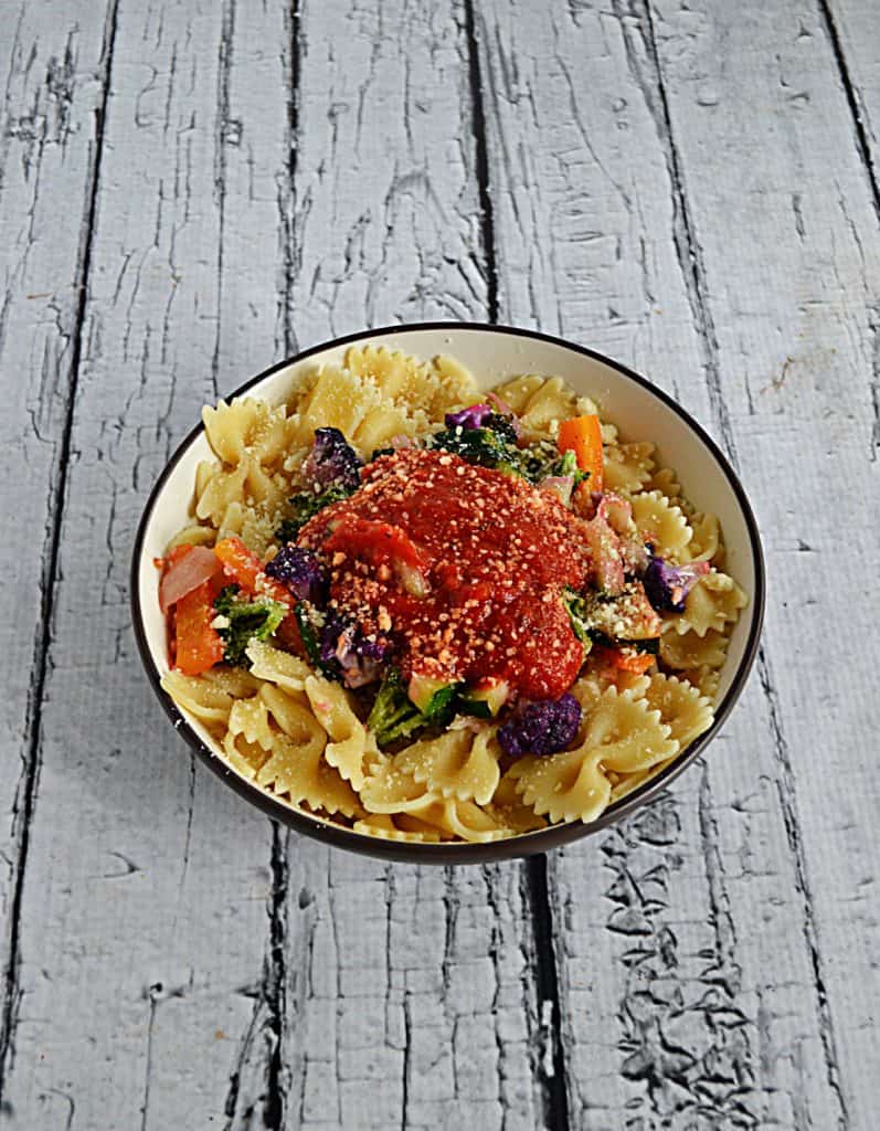 A side view of a bowl of bow tie pasta covered in sauteed vegetables and topped with a scoop of marinara sauce.