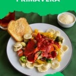 Pin Image: Title, A plate of ravioli and vegetables with sauce and a piece of garlic bread, a bowl of parmesan cheese and a glass of iced tea behind the plate.