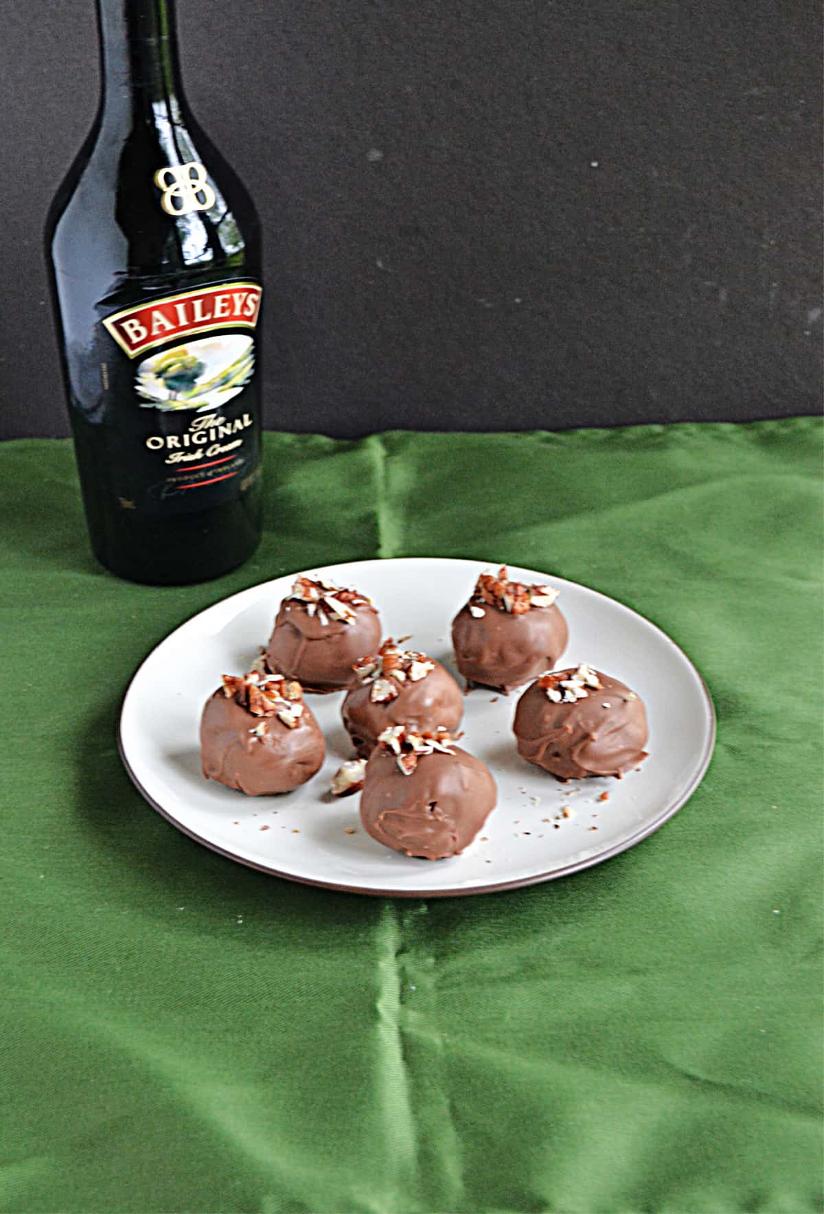 A plate of Bailey's truffles with a bottle of Bailey's Irish Cream behind it. 