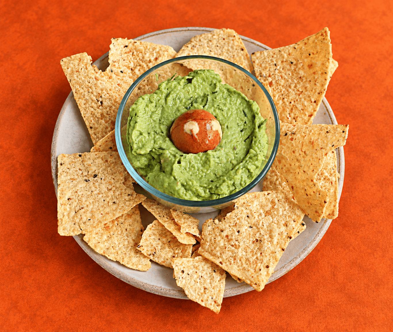 A plate of tortilla chips with a bowl of guacamole in the middle.