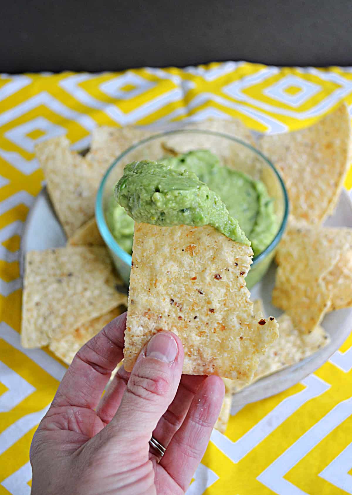 A hand holding a tortilla chip dipped in guacamole.