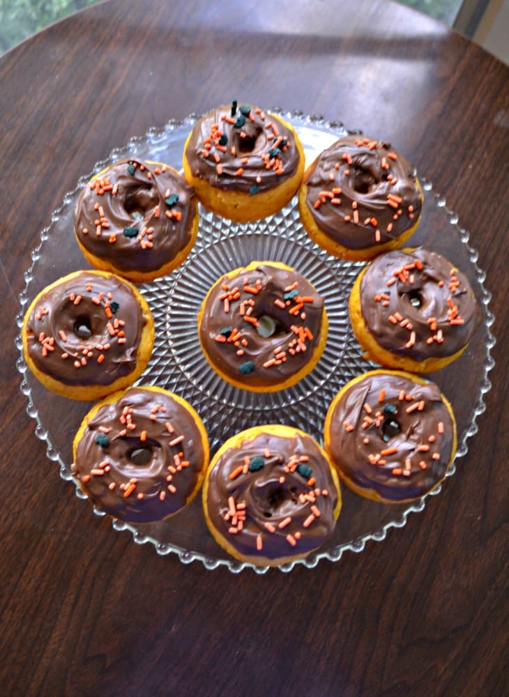 A glass plate topped with mini Pumpkin Donuts topped with chocolate glaze.