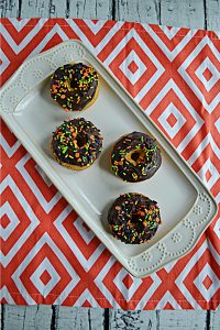 A platter with four baked pumpkin donuts topped with chocolate glaze and sprinkles.