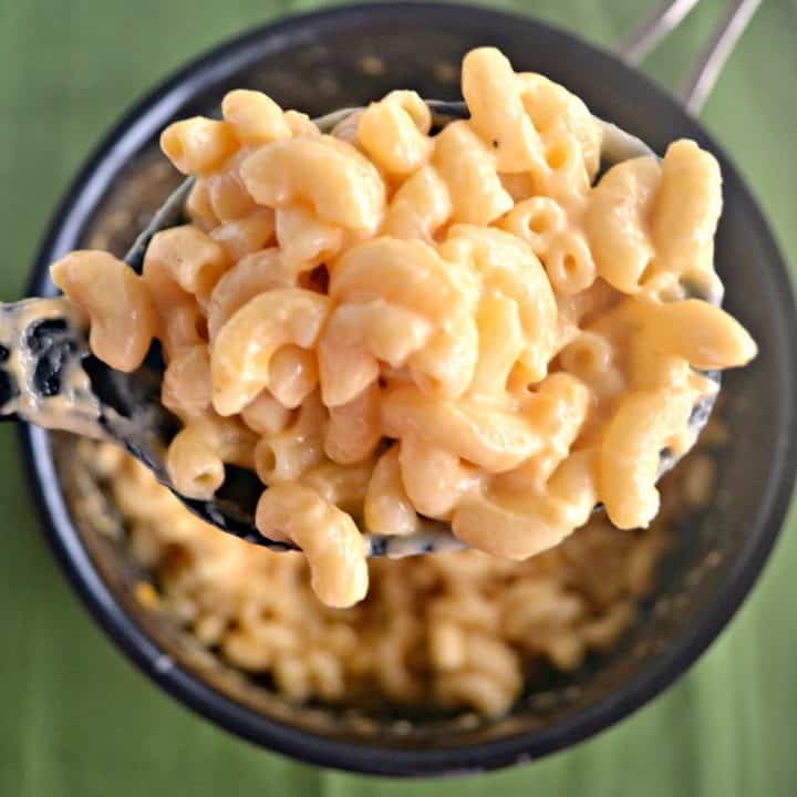 A pot full of macaroni and cheese with a large spoonful of it lose to the camera on a green background.