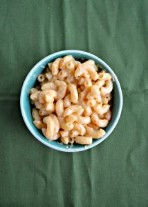 A small bowl filled with macaroni and cheese on a green background.