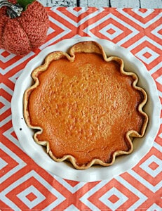 A pumpkin pie with a pumpkin behind it.