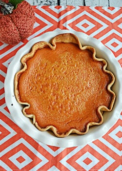 A pumpkin pie with a pumpkin behind it.
