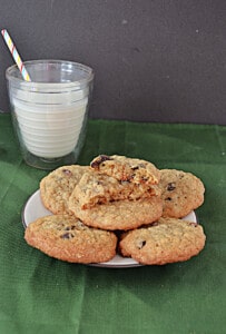 A plate of oatmeal raisin cookies with a cookie broke in half and a glass of milk behind the plate.