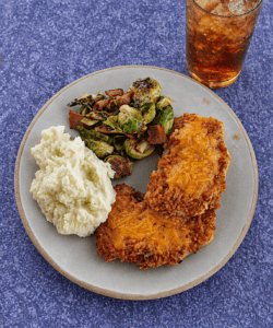 A plate with two pork chops, potatoes, Brussels Sprouts, and a glass of iced tea.
