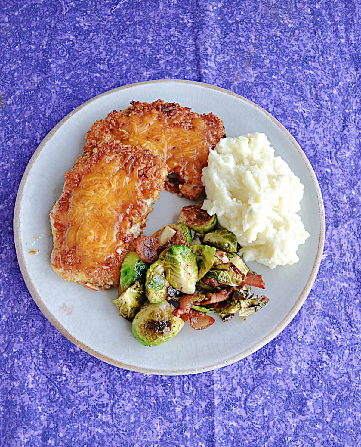 A plate with 2 cheesey pork chops, Brussels Sprouts, and a spoon of mashed potatoes.
