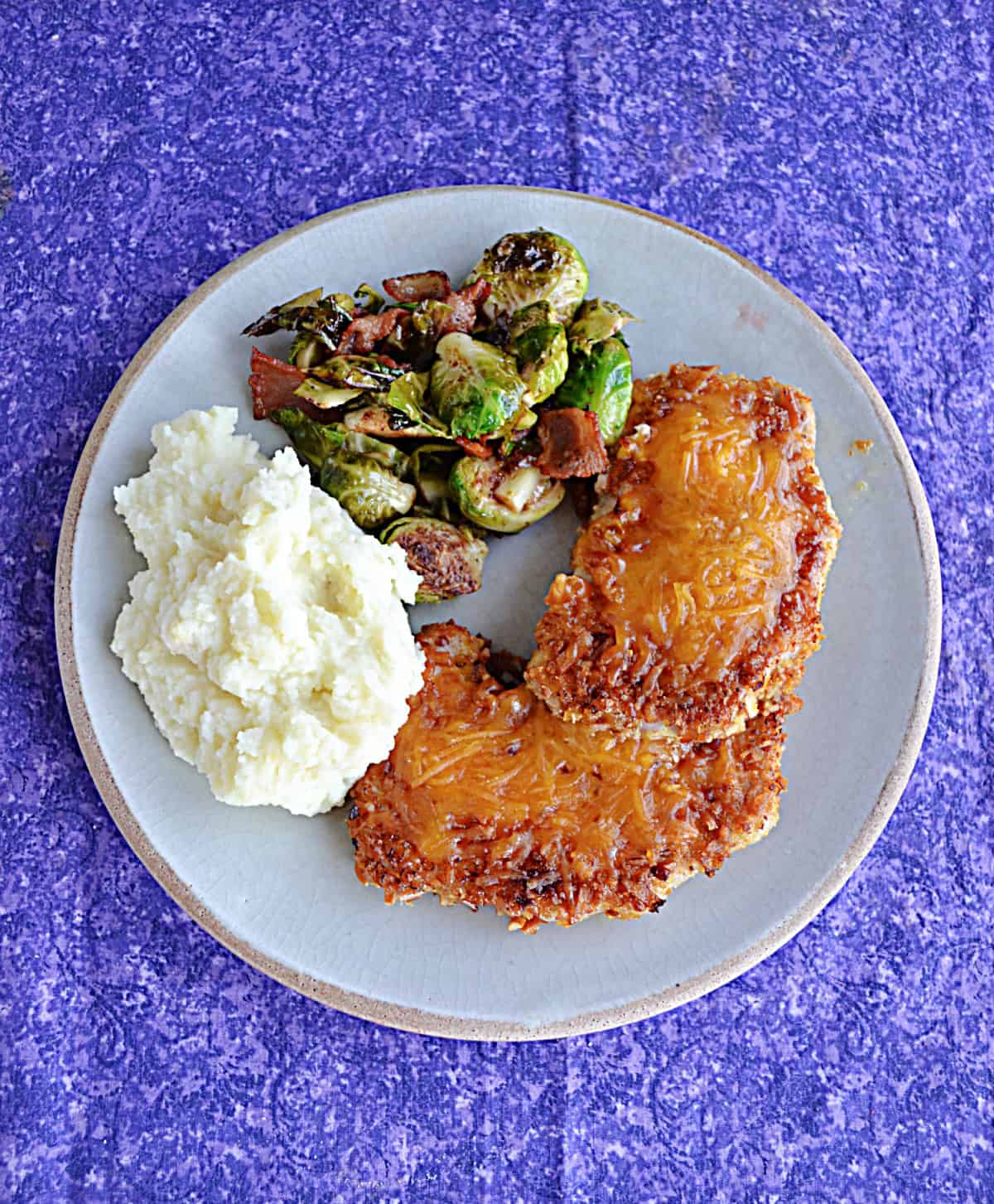 A top view of a plate of pork chops, mashed potatoes, and Brussels Sprouts.