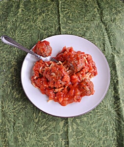 A plate of spaghetti and meatballs with marinara sauce and a fork picking up a meatball.