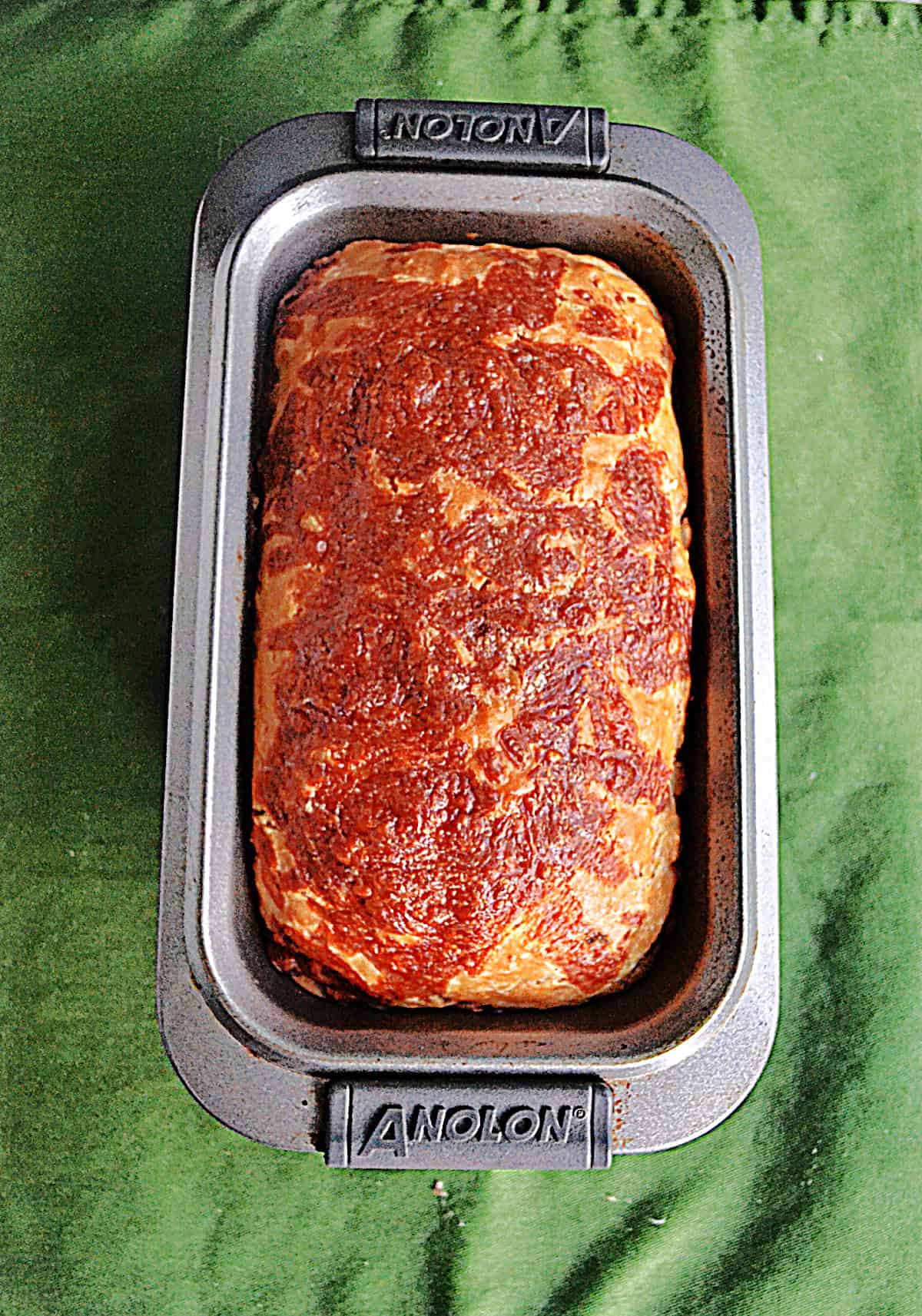 A loaf of golden brown bread in a bread pan with cheese on top.