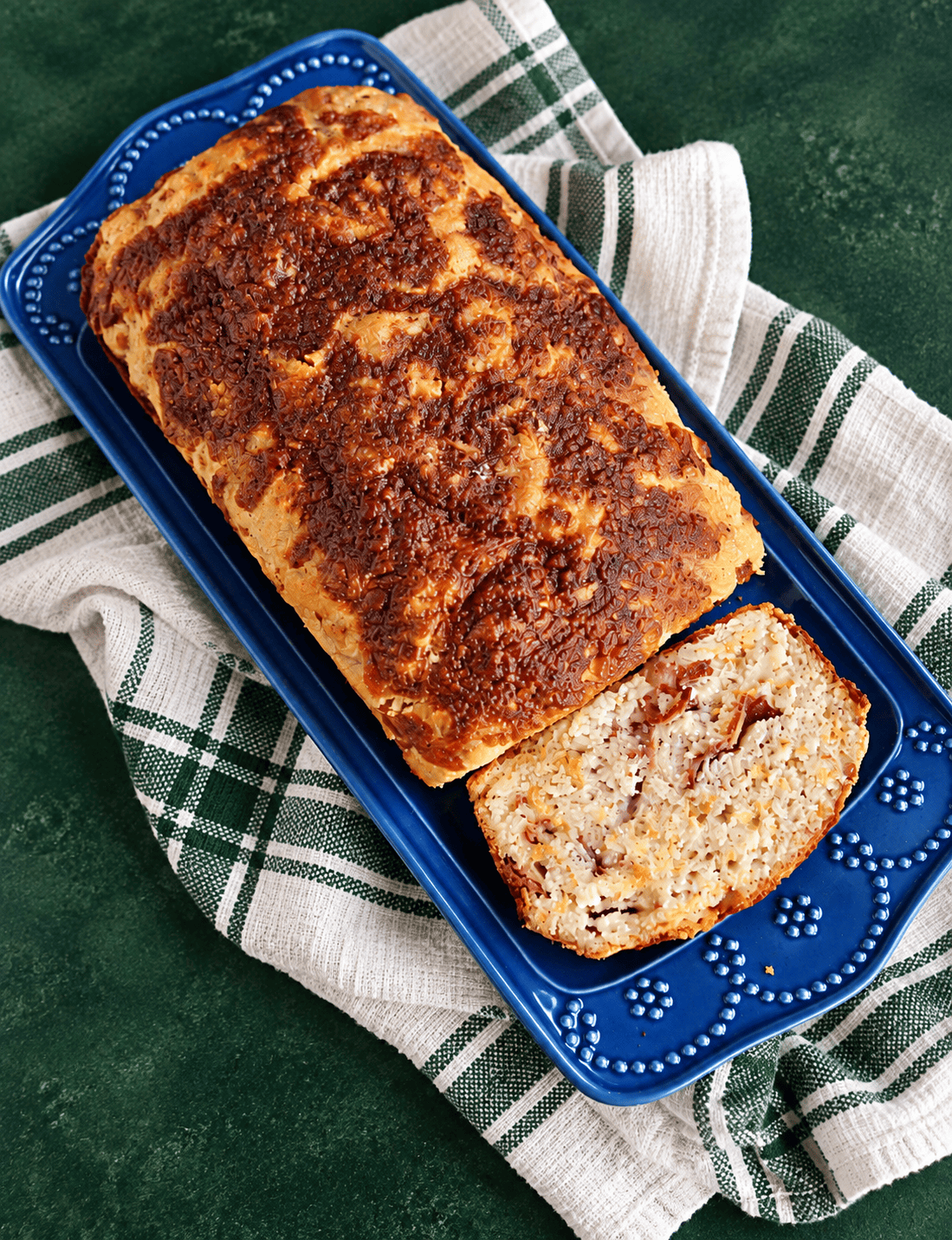 A loaf of cheddar bread on a blue platter on a dish towel.