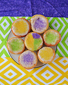 A plate of cupcakes topped with yellow, purple, and green sprinkles.