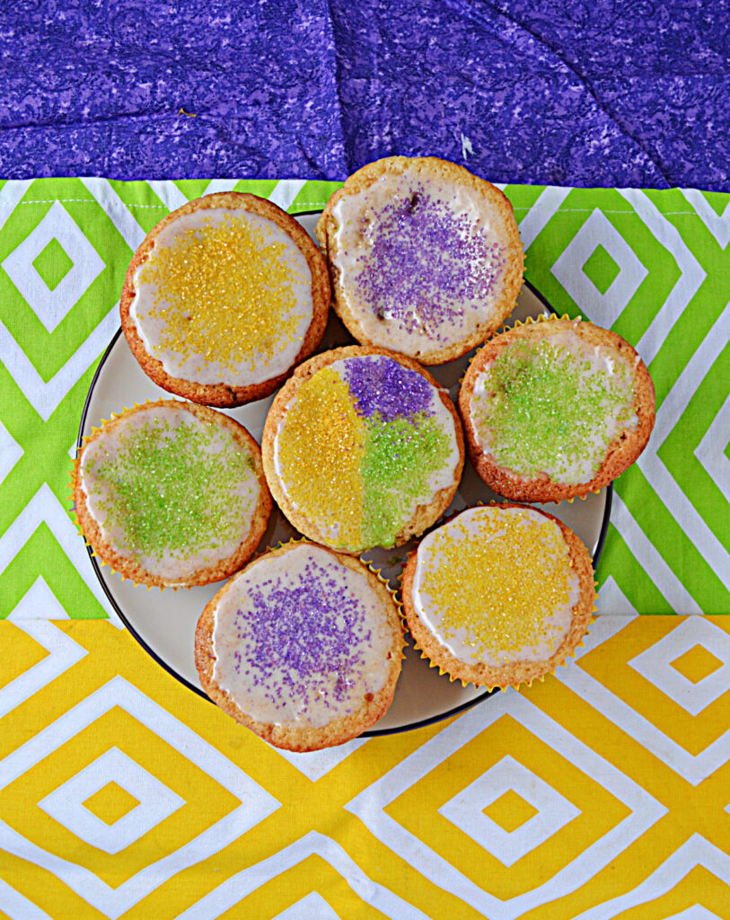 A plate of cupcakes topped with yellow, purple, and green sprinkles. 