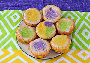 A close up of a plate of cupcakes topped with yellow, purple, and green sprinkles.