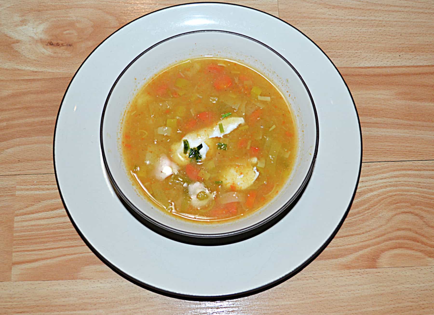 A top view of potato soup with sour cream and chives on top.