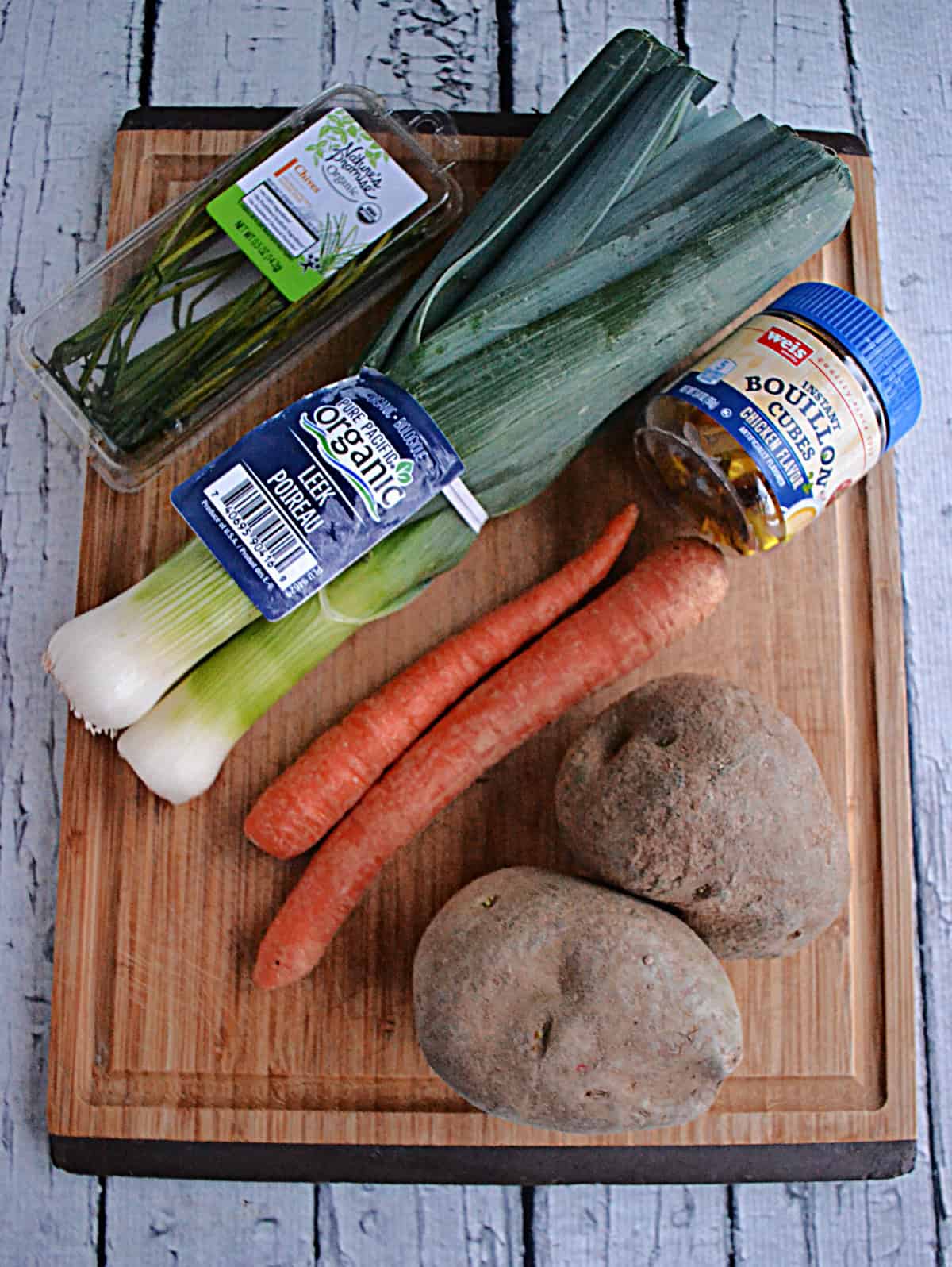Wooden cutting board with chives, carrots, potatoes, and leeks on it.