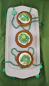 A platter with three green velvet cupcakes and green beads on it.