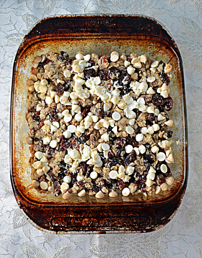 A baking dish with an oatmeal cookie base topped with cherries, apricots, and white chocolate chips. 