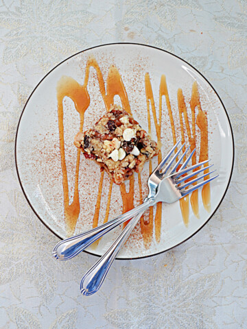 A top view of a plate topped with an Oatmeal Apricto Cherry Bar, drizzled in caramel sauce, with two forks on the plate.