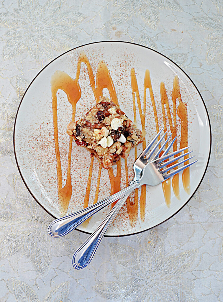 A top view of a plate topped with an Oatmeal Apricto Cherry Bar, drizzled in caramel sauce, with two forks on the plate. 