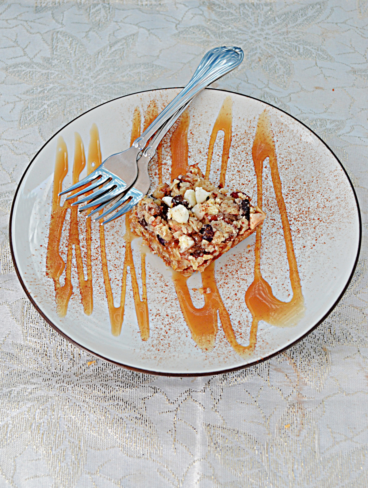 A plate topped with an Oatmeal Apricto Cherry Bar, drizzled in caramel sauce, with two forks on the plate.