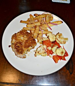 A dinner plate with a handful of french fries on the top, a golden brown pork chop to the left, and a mixture of cauliflower and red peppers to the right.