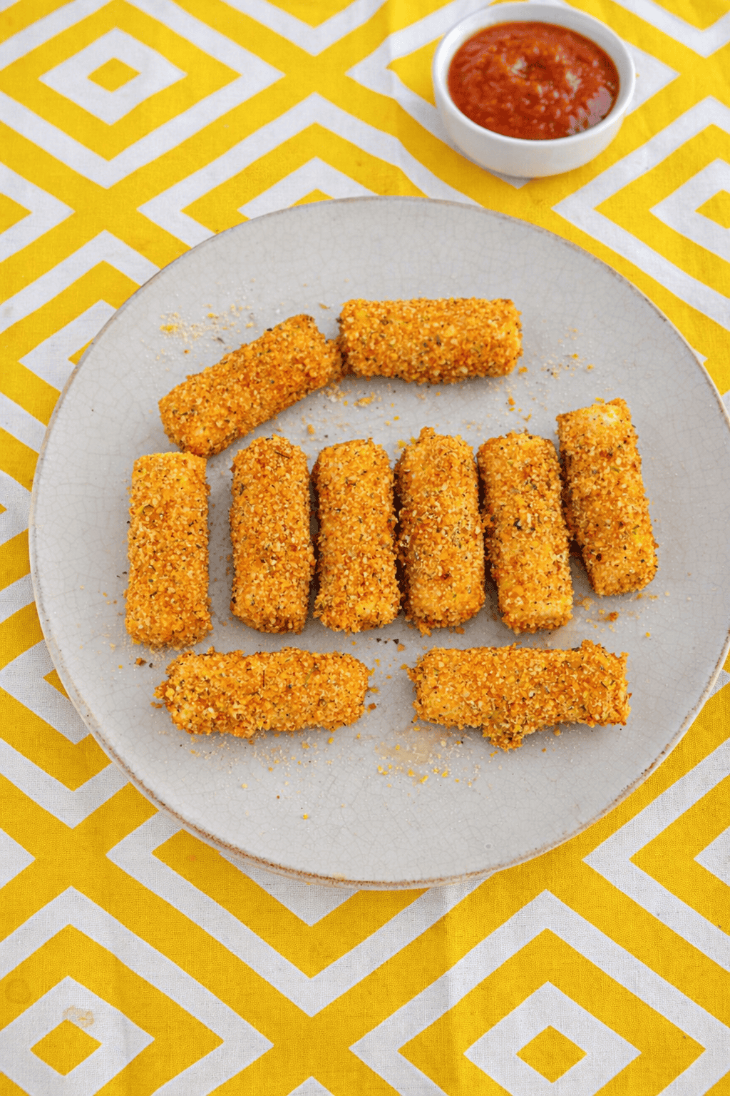 A plate of golden brown mozzarella sticks with a bowl of marinara in the background.