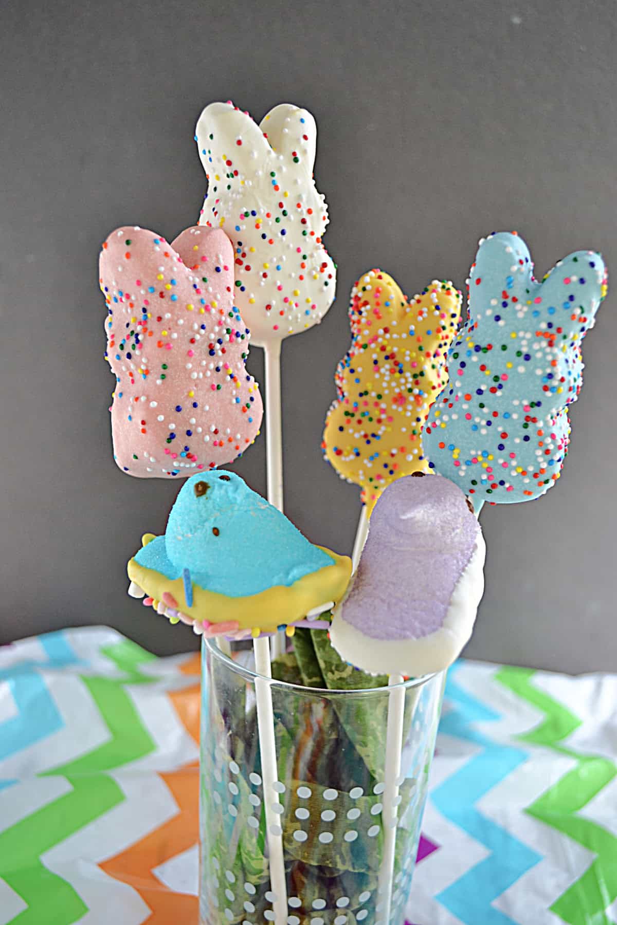 Chocolate covered peeps in pastel colors on sticks in a vase.