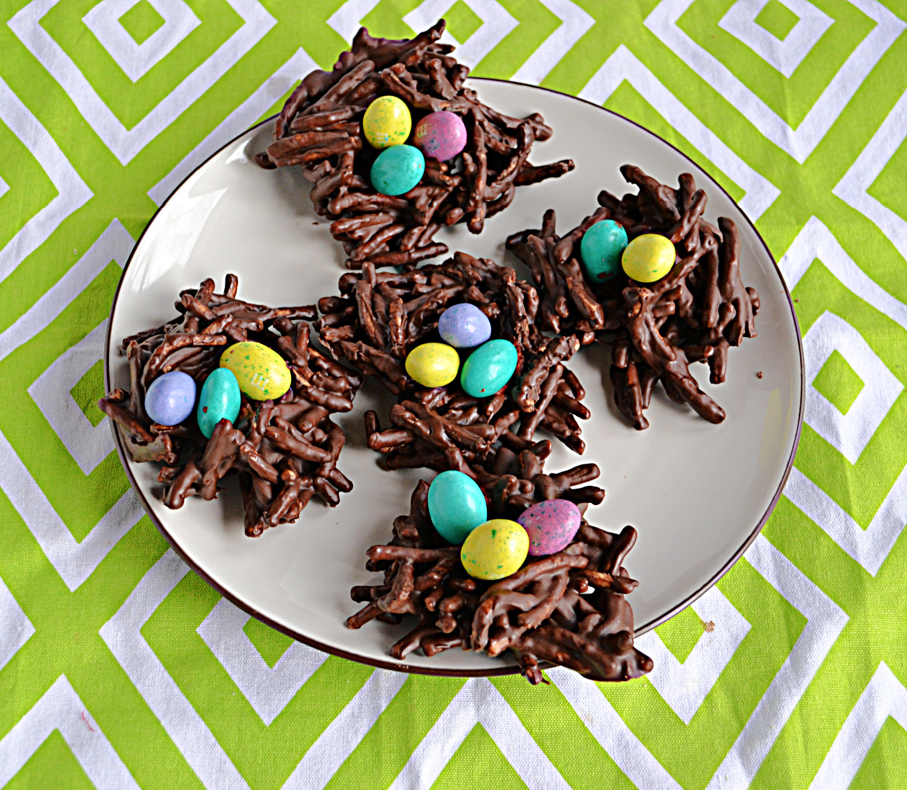 A plate of chocolate bird's nest cookies with candy coated eggs on top.