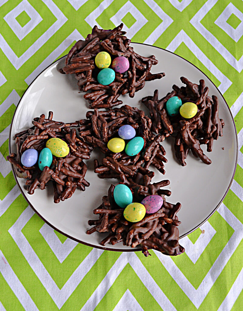 A plate of chocolate bird's nest cookies with pastel colored candy eggs on top. 